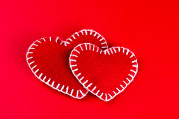 two decorative  hearts made of red fumirana sewn with a white thread, on a red background. Happy Valentine's Day symbol. selective focus. close-up. can be used as a background