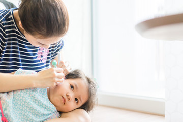Mother cleans her daughter ear with pincers.