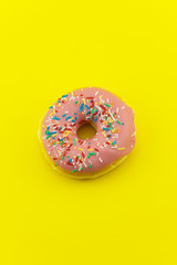 Close-up of a pink glazed donut isolated on yellow background. Strong candy contrast.