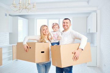Fototapeta na wymiar A happy family moves to a new apartment. Mother, father and child with boxes in the room of the new house.