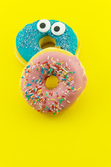 Close-up with many multicolored glazed donuts on yellow background.