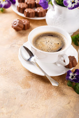 Holiday food composition with cup of cooffee, chocolate candies in flower shape and viola flowers. Postcard concept with copy space for text.