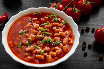 white beans in tomato sauce in a white bowl on dark wooden background