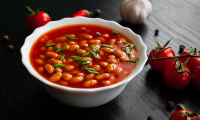 white beans in tomato sauce in a white bowl on dark wooden background