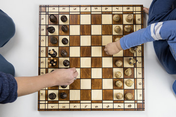 a top view of a child and an adult playing chess on white background