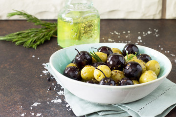 Olives, green olives with olive oil, fresh rosemary and spices on a stone or slate background.