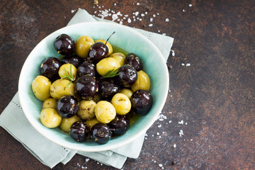 Olives, green olives with olive oil, fresh rosemary and spices on a stone or slate background.