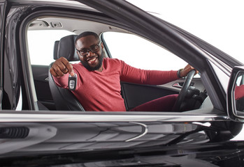 Fototapeta na wymiar Happy handsome african man showing car keys in his newly bought auto smiling cheerfully sitting in the luxury vehicle copyspace owner ownership sales driving consumerism private taxi concept
