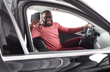 Happy handsome african man showing car keys in his newly bought auto smiling cheerfully sitting in the  luxury vehicle copyspace owner ownership sales driving consumerism private taxi concept