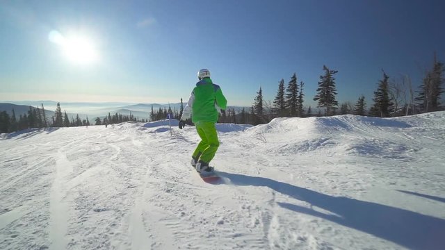 Sportsman drifts down on snowboard upon a slope of the hill at sunny winter day