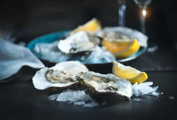 Schilderijen op glas Verse oesters close-up op blauw bord, geserveerd tafel met oesters, citroen en champagne in restaurant. Gourmet eten © Subbotina Anna