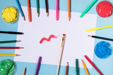 White sheet of paper on a blue background with a place to inscribe around a color pen ink painters and brushes, blue red yellow green paints and brash with red paint are painting