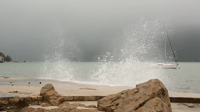 Storm on the sea. The wave breaks about the pier. Yacht in the background. Slow motion