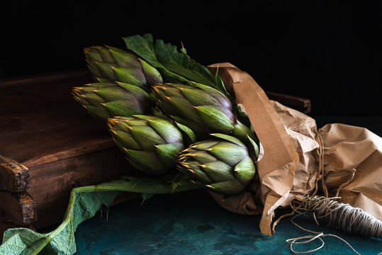 cinque carciofi e spago per legarli su sfondo rustico