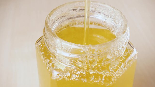Honey quickly pours into a glass jar and fills it
