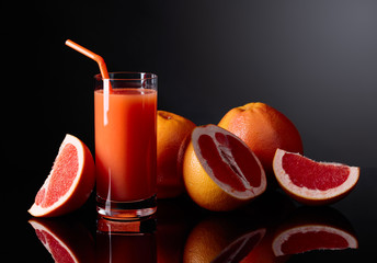 Glass of  grapefruit juice and cut fruits on black background.