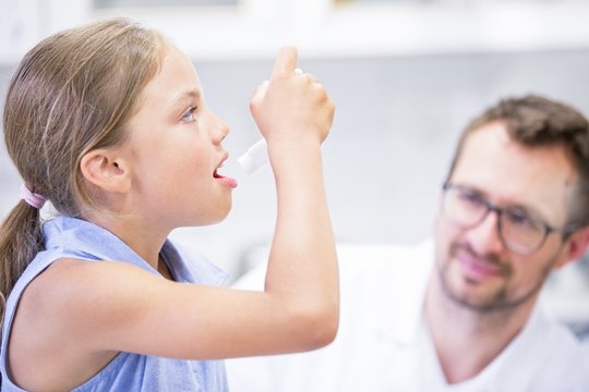 Girl using inhaler with doctor watching