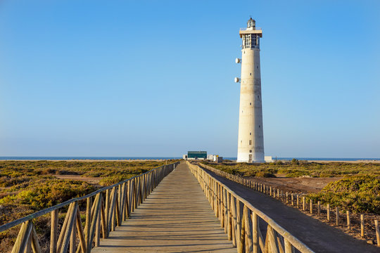 Wooden footbridge walkway to beach near Morro Jable lighthouse in warm sunset light, Fuerteventura island, Spain