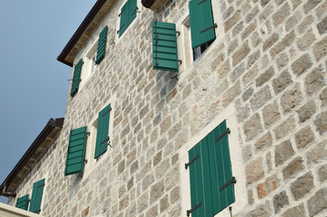Fototapeta na wymiar Open and closed wooden shutters on a house facade made of stone