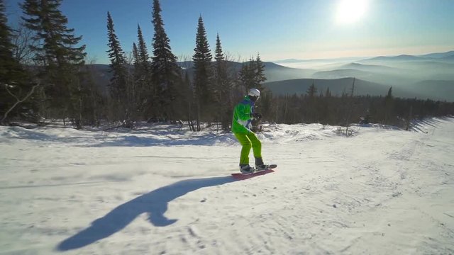 Sportsman moves down on extreme snowboard upon a slope of the mountain at sunny winter day