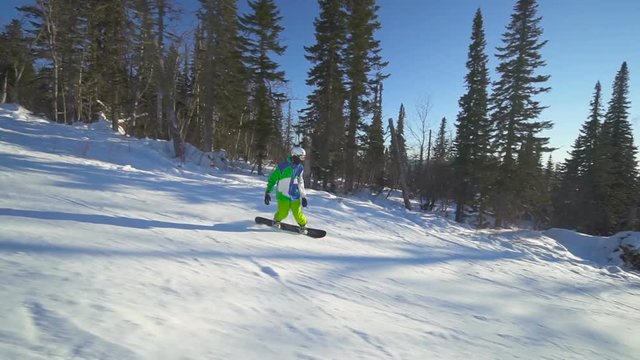 Sportsman is moving down on extreme snowboard upon a slope of the mountain at winter sunny day