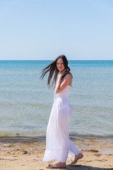 Fototapeta na wymiar Brunette woman in a white dress walks on the beach.