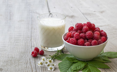 full bowl of juicy ripe raspberries next to a glass, decorated with chamomile flowers matricaria, perfect colorful summer background with wood texture, delicious light breakfast, still life