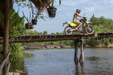 young man on cross motorbike crossing wooden bridge in jungle landscape -