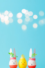 Easter holiday concept with cute handmade eggs: bunnies and chick. young branches green behind the ears. blue background, beautiful bokeh and copy space