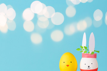 Easter holiday concept with cute handmade eggs: bunny and chick. young branches green. blue background, beautiful bokeh and copy space