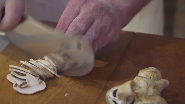 Professional man with chef cutting mushrooms on chopping wooden board with big knife. Kitchen concept.