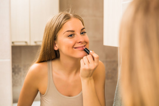 Beautiful woman applying lipstick  in the bathroom.
