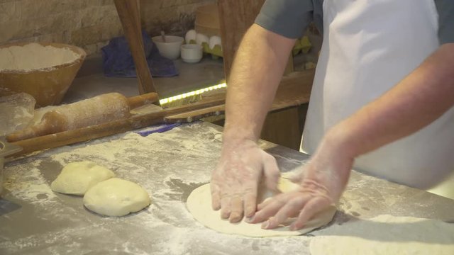 Making pizza or pide dough by close up male hands in pastry kitchen. Shaping dough is precursor to making a wide variety of food stuffs, particularly breads, biscuits, cakes, cookies, dumplings, pasta