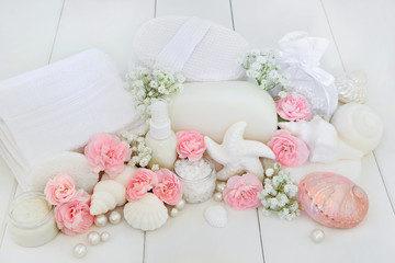 Spa and bathroom beauty treatment products with pink carnation and gypsophila flowers, ex foliating salt, shell soaps, body lotion, sponges, wash cloths, seashells and decorative pearls on white wood 