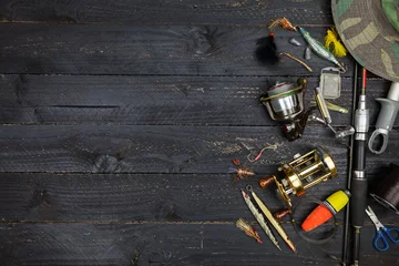 Cercles muraux Pêcher Cannes à pêche et moulinets, matériel de pêche sur fond de bois noir.