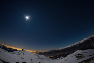 Turin city lights, night view from snow covered Alps by moonlight. Moon and Orion constellation,...