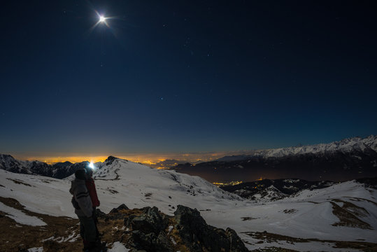 Moon and starry sky, snow on the Alps, fisheye lens. Orion Constellation, Betelgeuse and Sirio. Long exposure blurred two hikers looking at view, night outdoor activities.