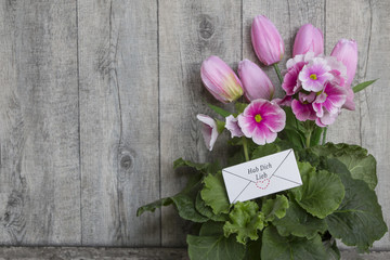 HAB DICH LIEB Brief mit Schriftzug in rosa Tulpen und Primeln vor grauer Holzwand