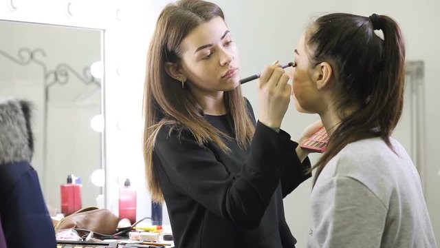 Visagist doing makeup for model girl in salon