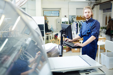 Confident young specialist carrying out his work in typography office by printing machine