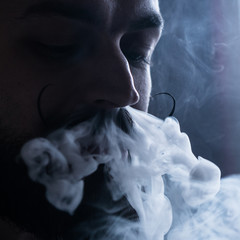 Man with Beard and Mustages Vaping an Electronic Cigarette. Vaper Hipster Smoke Vaporizer and Exhals Smoke Flow from Nose.