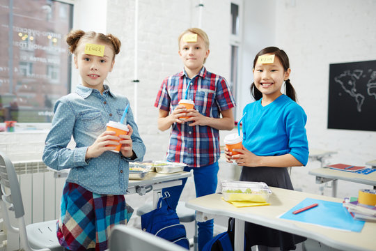Group of schoolkids with notepapers on their foreheads holding glasses with drinks