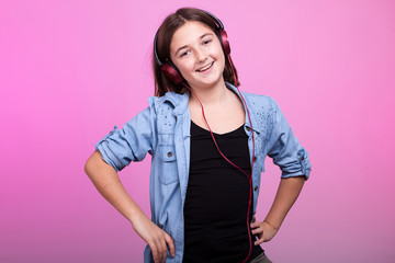Smiling young teenager girl listening to music on pink background in studio photo