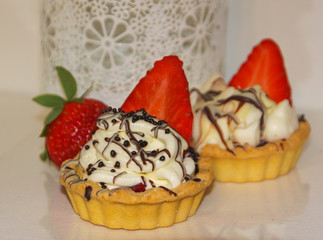 Appetizing tartlets with whipped cream and strawberries. Cream, chocolate and strawberries, a basket cake. white with red.