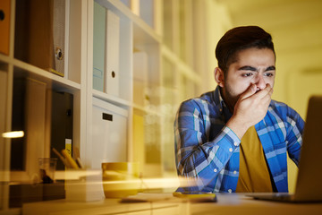 Worried guy covering mouth by hand while looking at laptop display and understanding that dangerous virus attacked his computer