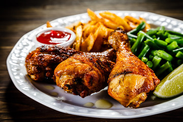 Grilled chicken drumsticks with vegetables on wooden background