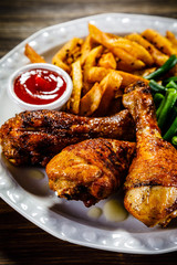 Grilled chicken drumsticks with vegetables on wooden background