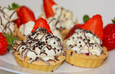 Appetizing tartlets with whipped cream and strawberries. Cream, chocolate and strawberries, a basket cake. white with red.