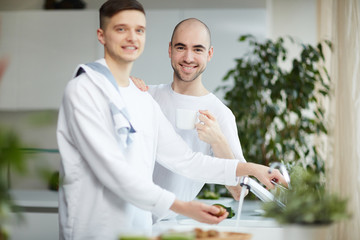 Two happy gay men in homewear spending morning in the kitchen