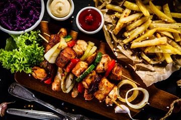 Kebabs - grilled meat with french fries and vegetables on wooden background 